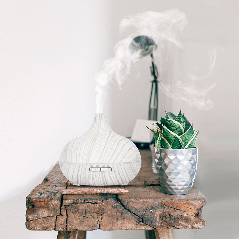 Stijlvolle aroma diffuser in witte houtlook met een sierlijke ronde vorm, inclusief afstandsbediening. Met instelbare timer (1u, 3u, 6u) en sfeervolle LED-verlichting
